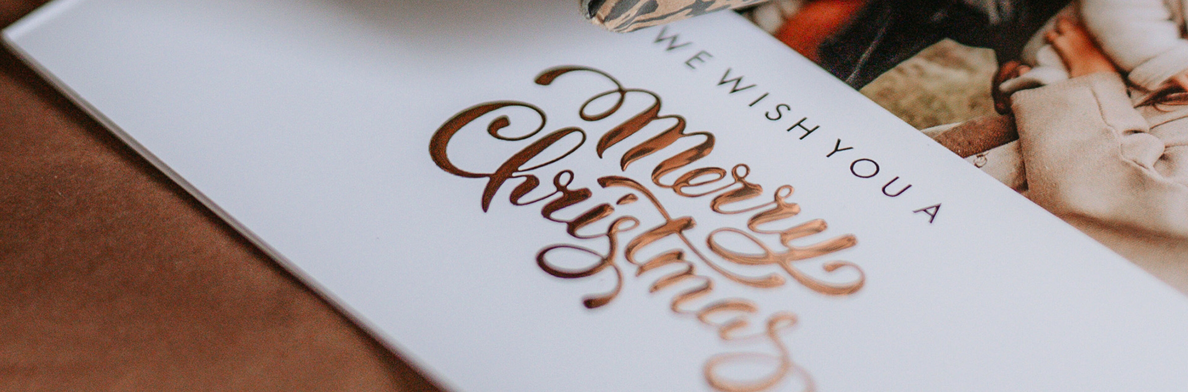 Hand met tatoeage houdt een glanzende kerstkaart met de tekst 'We wish you a Merry Christmas'.