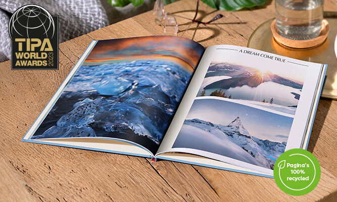 Een open CEWE FOTBOEK met landschapsfoto's op een houten oppervlak.